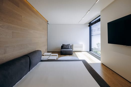 The space is a cozy bedroom featuring a comfortable bed, a stylish chair, a television for entertainment, and a large window that brings in natural light