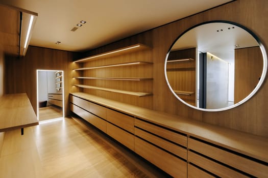 Theres a spacious walkin closet featuring elegant wooden shelves expertly crafted, accompanied by a beautiful round mirror enhancing the overall aesthetics