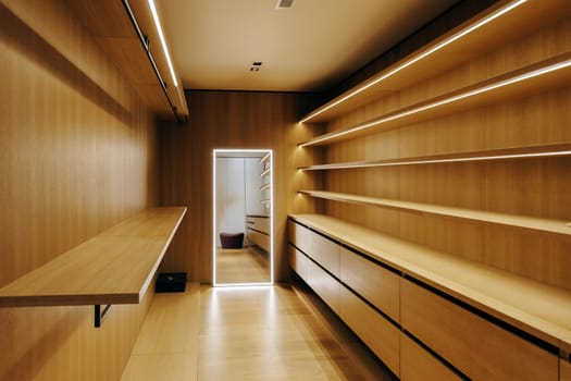 A spacious walkin closet that features beautifully crafted wooden shelves along with organized drawers for ample storage and style