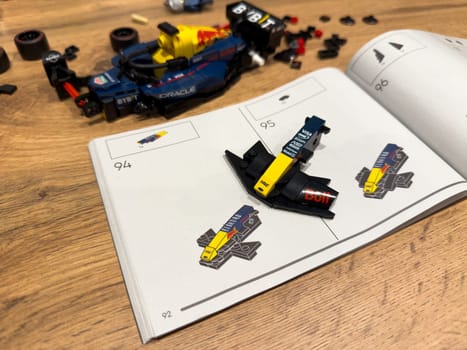 Moscow, Russia, April 26, 2025: Close up of the front wing module from LEGO Speed Champions Red Bull Racing Formula 1 car 2024. Shown mid assembly above printed instruction steps on wooden surface