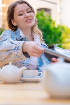 Caucasian woman smiling as she pays with a credit card using contactless technology at an outdoor cafe. A casual urban moment reflecting convenience, lifestyle, and modern financial habits. Vertical