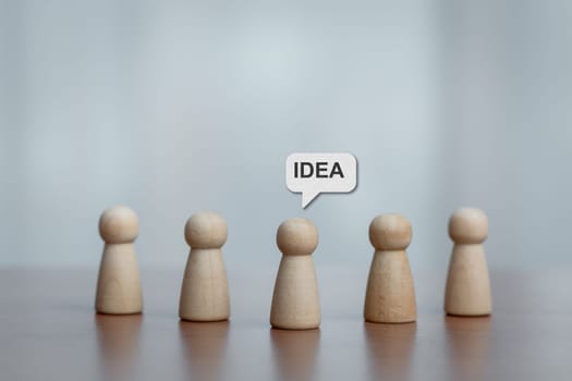 Five wooden figurines standing together, center figure with 'IDEA' speech bubble. Concept of brainstorming, teamwork, leadership, creativity, and innovation.