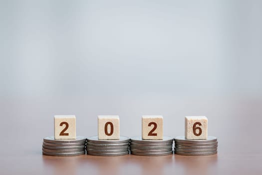 Stacked coins supporting wooden blocks with '2026'. Concept of financial growth, future planning, investment, savings, and economic goals.