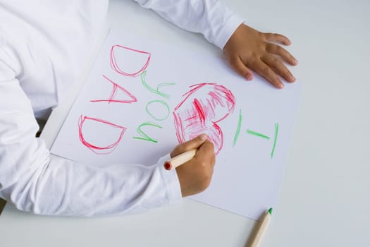Child drawing heartfelt message with crayons for dad on white paper surface. Father day.
