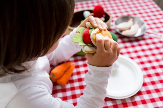 Child engages in imaginative play with toy food at a checkered table.