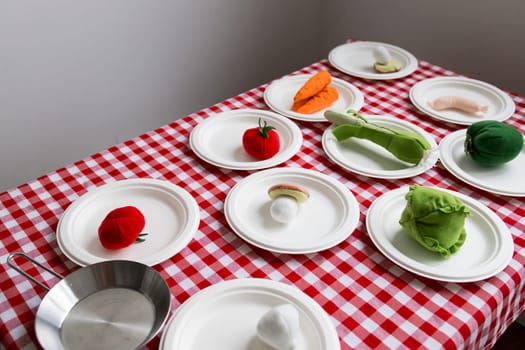 Colorful plush vegetables on checkered tablecloth with white plates.