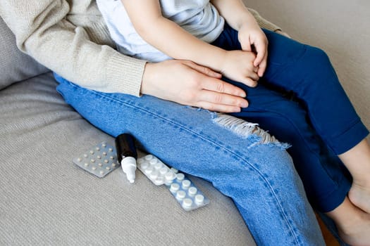 Mother comforting child on couch with pills and nasal spray nearby.