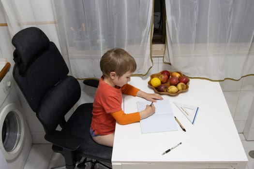 Young child drawing on notebook while sitting on an ergonomic chair at kitchen table