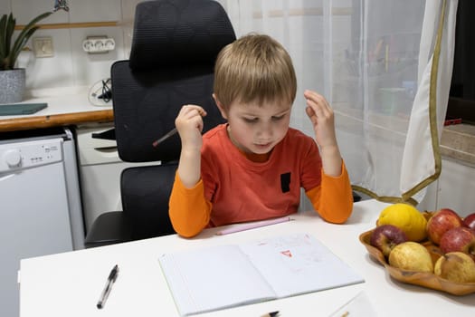 Young boy concentrating on his homework, holding a pencil and thinking, sitting at the kitchen table