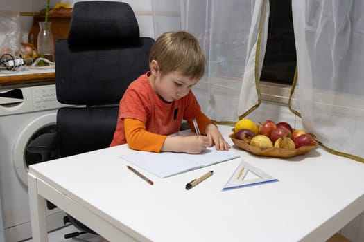 Child studying and writing on a notebook, sitting at a white table, with some fruit nearby