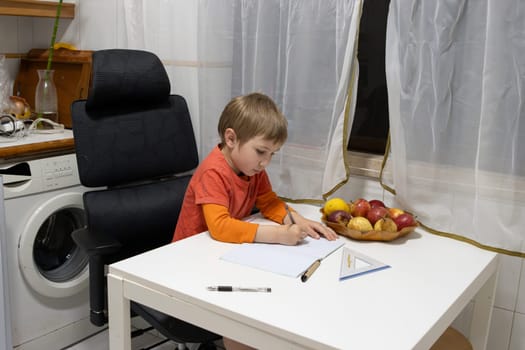 Boy drawing and learning at home, sitting at kitchen table next to washing machine