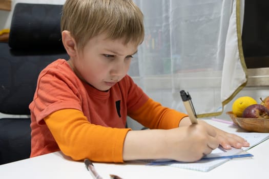 Concentrated pupil writing on notebook, doing homework at home