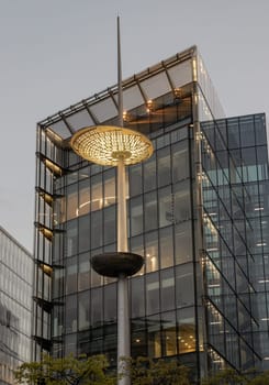 London, UK - Apr 27, 2025 - View of light pole in front of glass modern building on the Southbank after sunset in City of London. The spear like pole has two concentric disks, use it as your Wallpaper, Poster and Space for text, Selective focus.