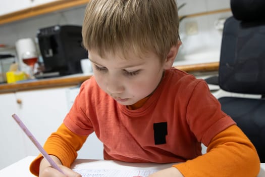 Preschool boy drawing with colored pencil on squared paper, developing his fine motor skills in a domestic setting