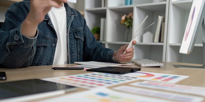 A creative individual evaluates various color options and layouts using a digital tablet and printed swatches in a modern workspace.