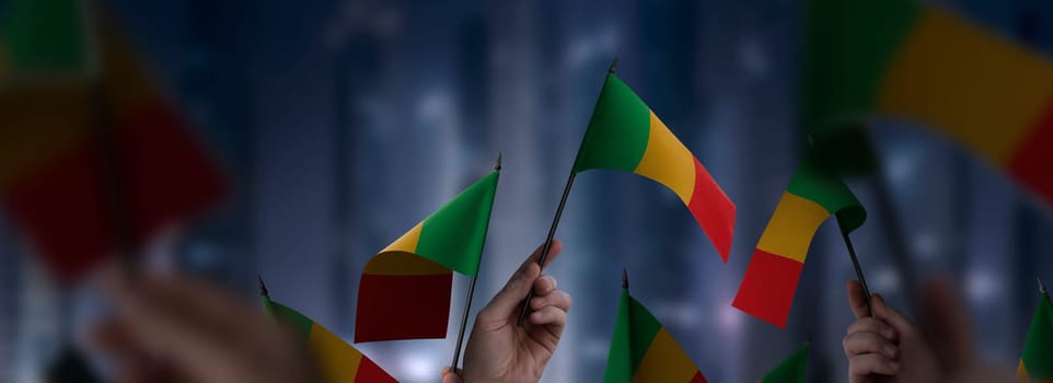 Mali flags in their hands on a blurred urban background. The photo illustration was created without the use of artificial intelligence, only using Photoshop.