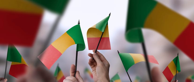 Mali flags in their hands on a blurred urban background. The photo illustration was created without the use of artificial intelligence, only using Photoshop.