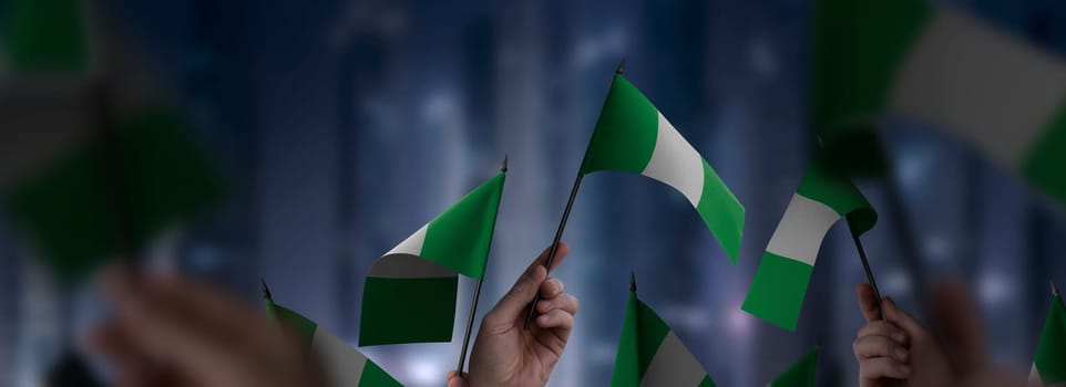 Nigeria flags in their hands on a blurred urban background. The photo illustration was created without the use of artificial intelligence, only using Photoshop.