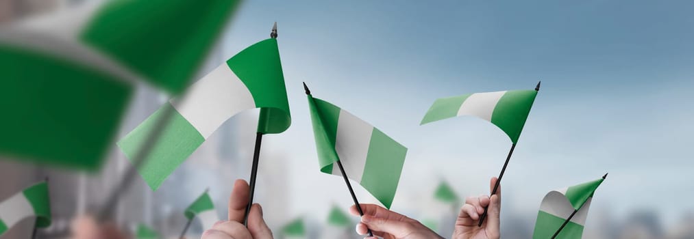 Nigeria flags in their hands on a blurred urban background. The photo illustration was created without the use of artificial intelligence, only using Photoshop.