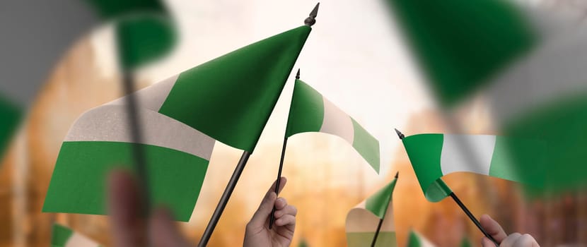 Nigeria flags in their hands on a blurred urban background. The photo illustration was created without the use of artificial intelligence, only using Photoshop.