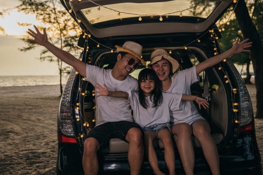 Asian family sitting back car to beach at sunset feeling funny in holidays and relaxation together. Dad, mom and daughter happy weekend travel enjoy at beach. summer vacation travel camping road trip