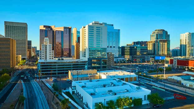 Aerial view of downtown Phoenix Arizona at golden hour with modern high-rise buildings like Courtyard by Marriott and US Bank tower glowing in sunlight against a backdrop of clear sky and distant mountains