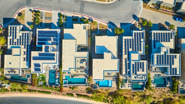 Aerial view of modern Lake Las Vegas homes with flat roofs and solar panels, private blue pools, and drought-tolerant landscaping in a sunny Nevada suburb, showcasing eco-friendly luxury living