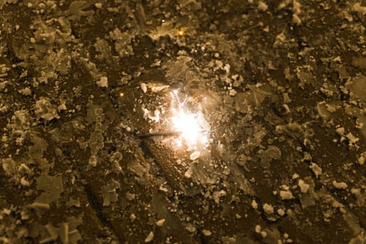 Sparkler burns on winter pavement. Concept of celebration, magic, fleeting moment in urban setting.