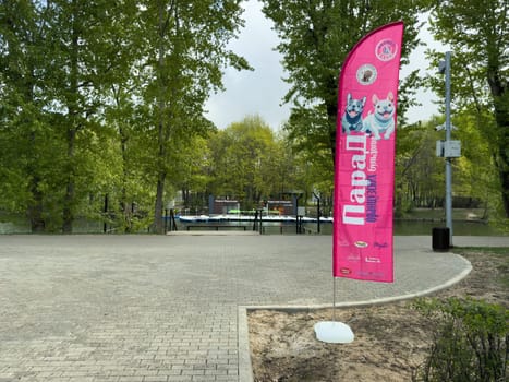 Moscow, Russia, April 27, 2025: Bright pink banner promoting the French Bulldog Parade in Vorontsovsky Park, placed near the lake and boat rental area in scenic green environment