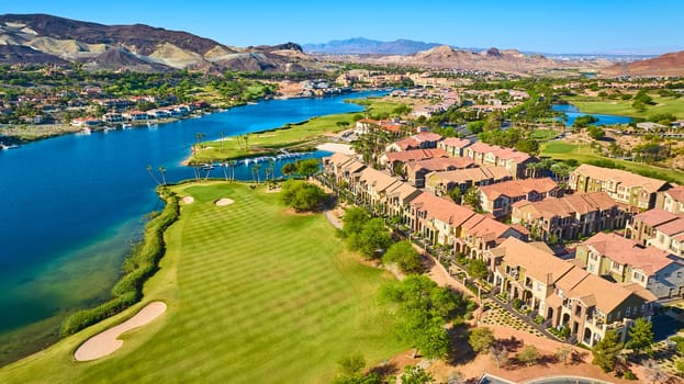 Aerial view of a luxury lakeside community in Lake Las Vegas Nevada featuring a lush golf course sparkling blue water and upscale townhomes surrounded by desert mountains on a bright sunny day