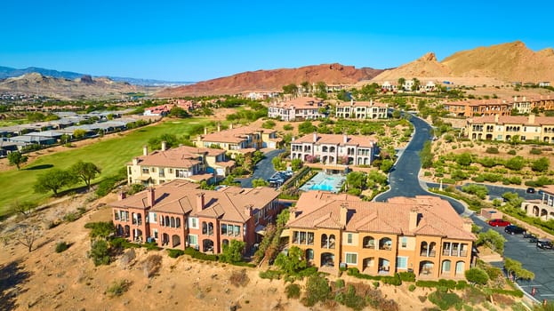 Aerial view of luxury Mediterranean villas in Lake Las Vegas Nevada with manicured gardens a central pool and a lush golf course surrounded by desert mountains under a clear blue sky