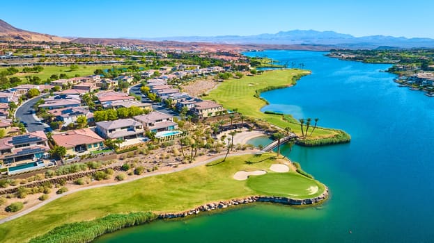 Aerial view of a luxury lakeside golf community in Lake Las Vegas Nevada featuring modern homes manicured fairways sparkling blue water and scenic desert mountains under sunny skies