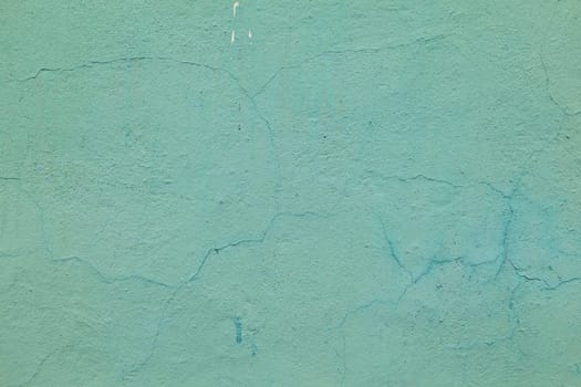 Abandoned concrete wall with damaged turquoise paint, small cracks. A weathered wall damaged by time.