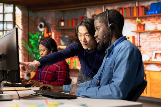 Asian call center senior manager providing guidance to multiethnic team, addressing questions. Customer support workplace onboarding specialist conducts orientation sessions for multiracial coworkers