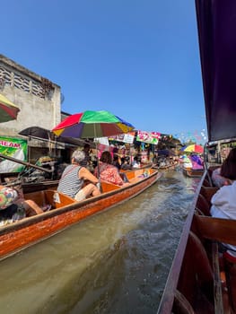 Bangkok, Thailand - November 12, 2024: Tourists group on boats visit the floating market to buy produce and traditional exotic Thai food from bazaar while sitting in sailboats on the canal.