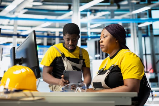 Photovoltaics factory supervisors evaluating performance of robot arms placing solar panels on assembly lines, producing sustainable energy. All black team looking at the production process.