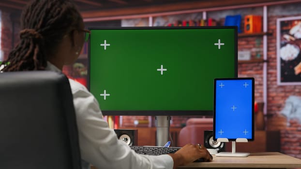 Freelancer in home office using green screen PC and mockup tablet to work on job tasks. Teleworker using chroma key computer monitor and isolated screen device to do job online