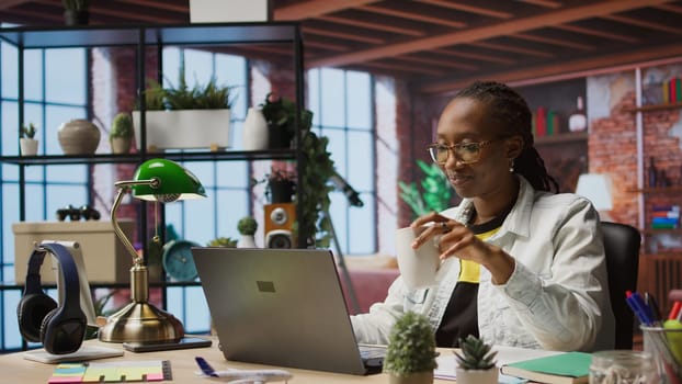 Woman enjoying leisure time at home, drinking coffee, texting friends on laptop. Cheerful person talking with mates on social network online website, using notebook, camera A