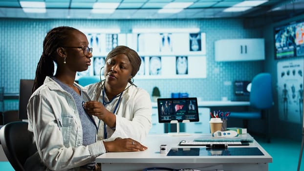 General practitioner uses a stethoscope to consult patient with illness, ensuring normal function of lungs and heartbeat. African american girl with a respiratory problem at checkup. Camera B.