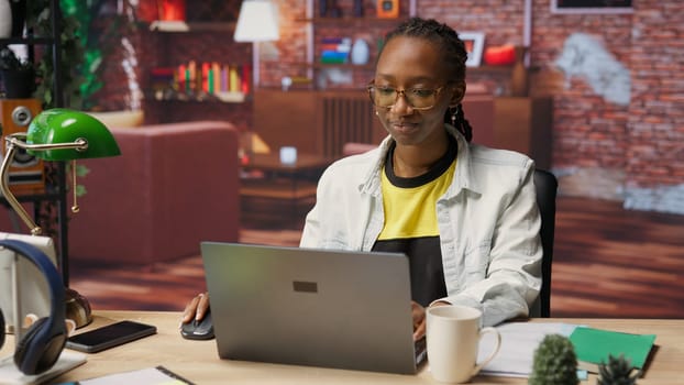 Student at home drinking coffee and browsing internet on notebook, researching information online. Woman enjoying hot beverage while reading internet articles on laptop for school tasks, camera B