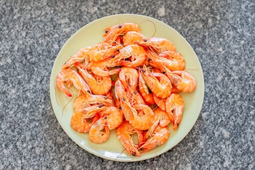 Cooked shrimps are arranged on a light green plate placed on a granite countertop, ready to be enjoyed as a delicious seafood meal or appetizer