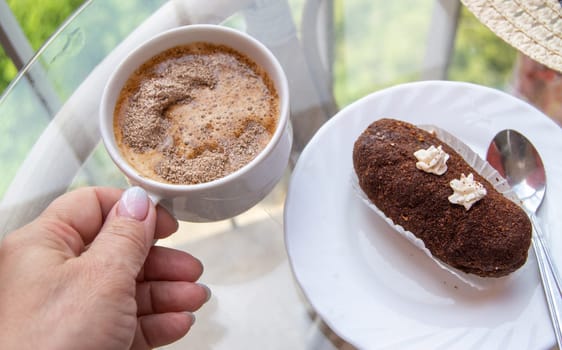 Female hand holding a cup of espresso coffee near a plate with chocolate brownie. Breakfast concept.