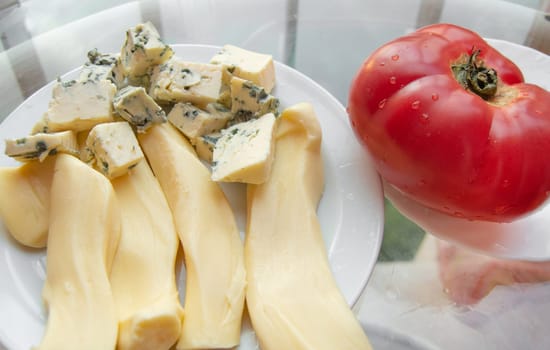 Different kinds of cheese on the plate and one red tomato, appetizers.