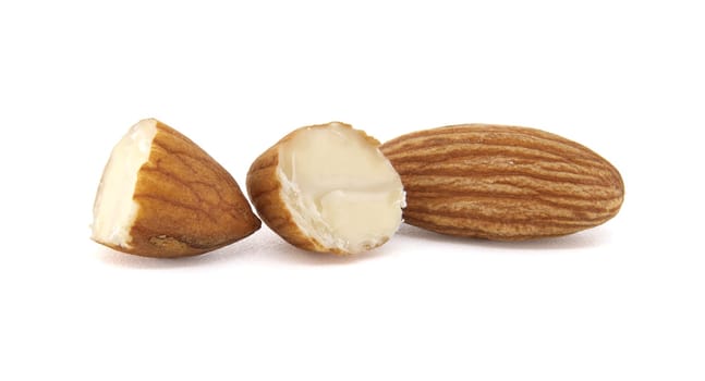 Close-up shot of three almonds against a bright white background, showcasing detail. One is whole, two are broken open to display the interior.