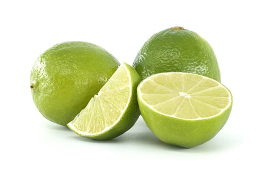 Two whole limes and a half lime and a lime wedge are creating a composition on a white background, showing the freshness of the fruit and the juicy interior