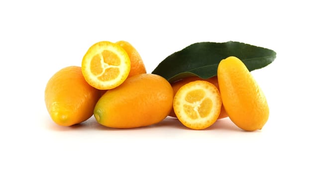 Several ripe kumquats, whole and cut, with a vibrant green leaf, create a colorful display on a plain white backdrop, emphasizing the freshness and natural beauty of these small citrus fruits