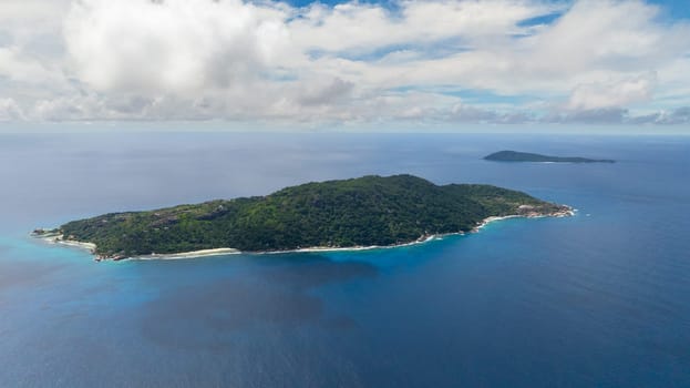 A distant island surrounded by deep blue ocean and greenery under a cloudy sky. Felicite, Seychelles.