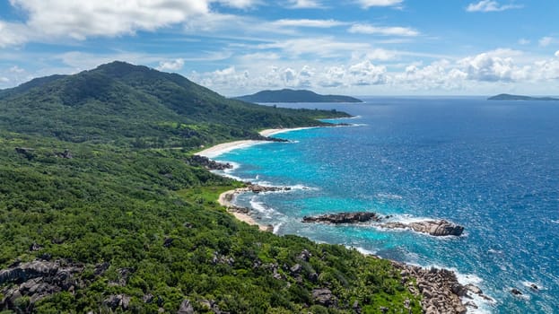 Waves roll onto the shore, hitting rocky formations with tropical greenery. La Digue, Seychelles.