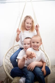 Three cheerful kids are enjoying their time on a cozy swing, sharing laughter and fun in a lively indoor space.