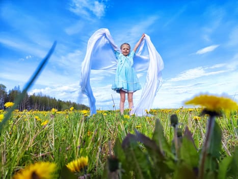A child with flowing fabric enjoys a breezy moment, surrounded by vibrant dandelions under a clear blue sky.